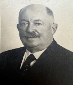 A person with a mustache wearing a suit and tie

Description automatically generated
